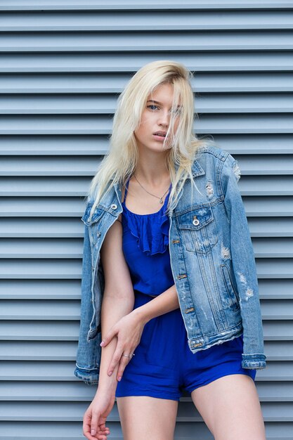 Straat fotosessie van glamour blonde vrouw draagt casual kleding poseren in de buurt van de metalen luiken