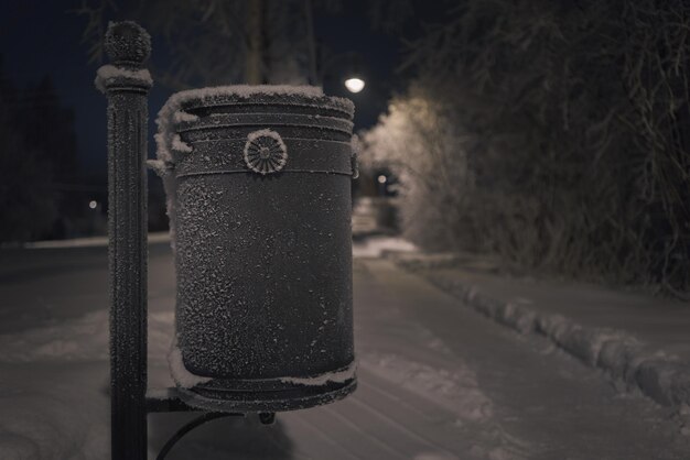 Straat gietijzeren prullenbak bedekt met vorst en sneeuw. Winter nacht