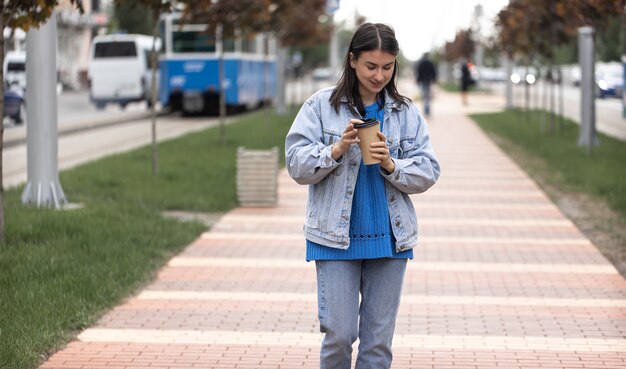 Straatfoto van een aantrekkelijke jonge vrouw die langs een stadsstraat loopt met een kopje koffie in haar hand.