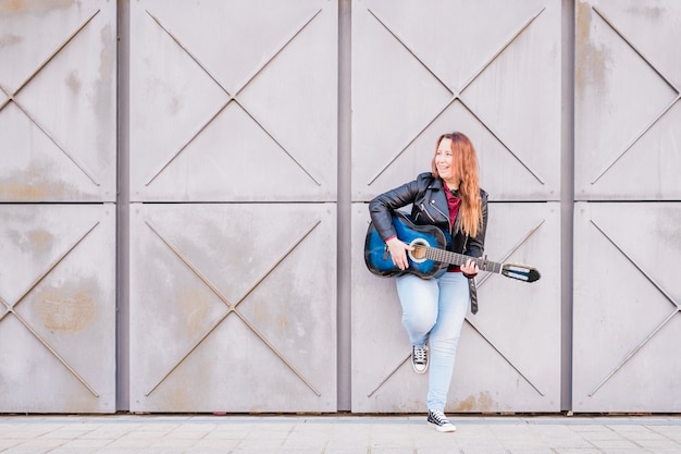 Straatmuzikant die akoestische gitaar speelt jonge vrouw die buiten een jas draagt