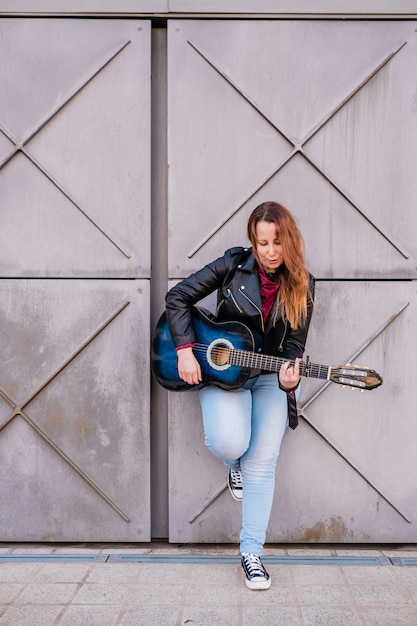 Straatmuzikant die akoestische gitaar speelt Jonge vrouw die buiten een jas draagt