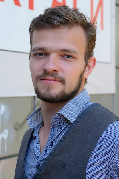 Straatportret van een jonge knappe man met een kleine baard en snor in een vest op een warme zomerdag