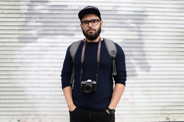 Straatportret van een mannelijke fotograaf met een baard in een bril en een pet met een vintage fotocamera