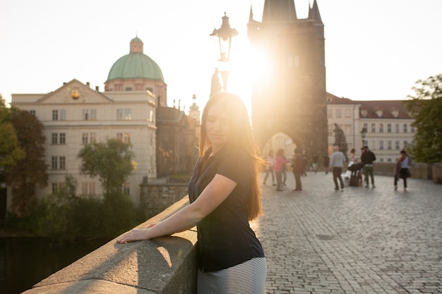 Straatportret van een schattige brunette vrouw met lang haar die zich voordeed op de brug in zonnestralen