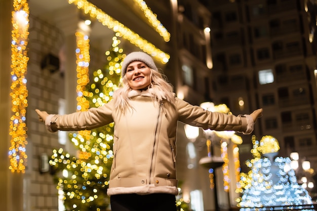 Straatportret van lachende mooie jonge vrouw op de feestelijke kerstmarkt. dame die klassieke stijlvolle wintergebreide kleding draagt.