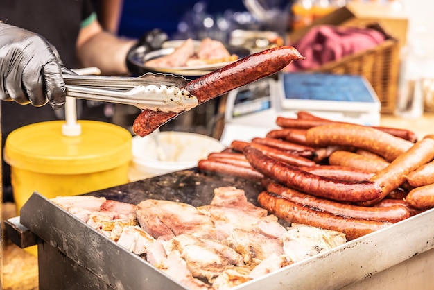 Straatverkoper houdt grote worst vast met een tang tijdens een verkoop op de straatvoedselbeurs