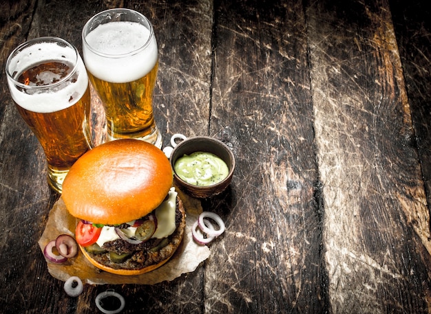 Straatvoedsel Een grote hamburger met glazen licht bier op een houten achtergrond