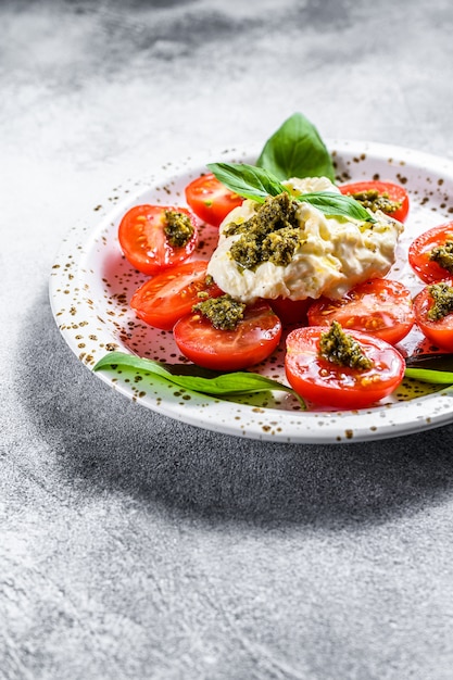 Stracciatella on small plate served with fresh tomatoes and basil.