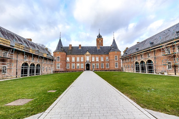 Straight path in outer courtyard in direction of Alden Biesen Castle between side buildings rear facade brick walls gable roof and two towers 16th century cloudy day in Bilzen Limburg Belgium