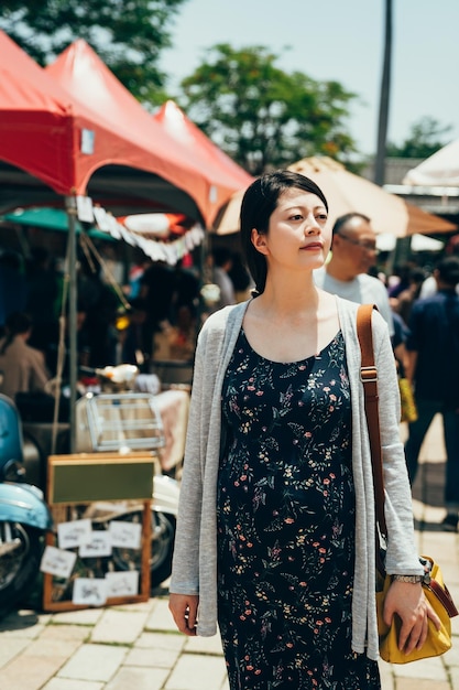 젊고 우아한 아시아 일본 임산부의 직선 사진은 화창한 날씨에 야외 시장을 산책하며 휴식을 취합니다. 화창한 플레어에 현지 장소에서 큰 복부 쇼핑을 가진 행복한 미래의 어머니.