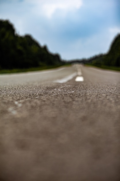 Straight road with a marking on the nature background. Open Road in future, no cars, auto on asphalt road through green forest, trees. Clouds on blue sky in summer, sunshine, sunny day. Bottom view