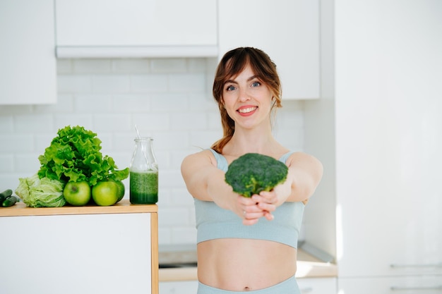 Stralende jonge vrouw met een broccoli in volledig uitgestrekte handen glimlachend