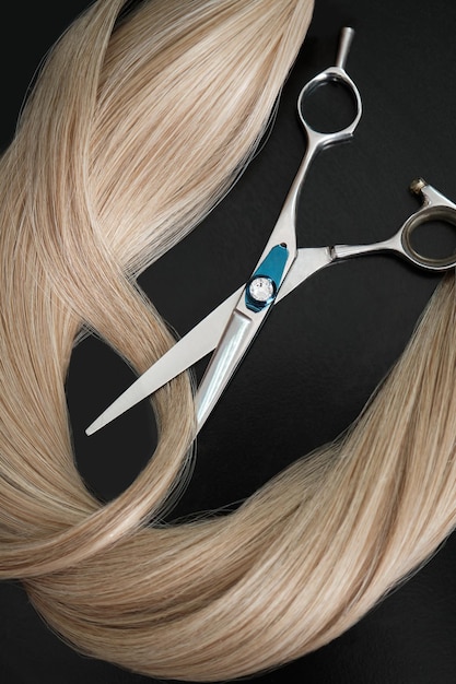 A strand of blond hair with scissors on a black background Closeup