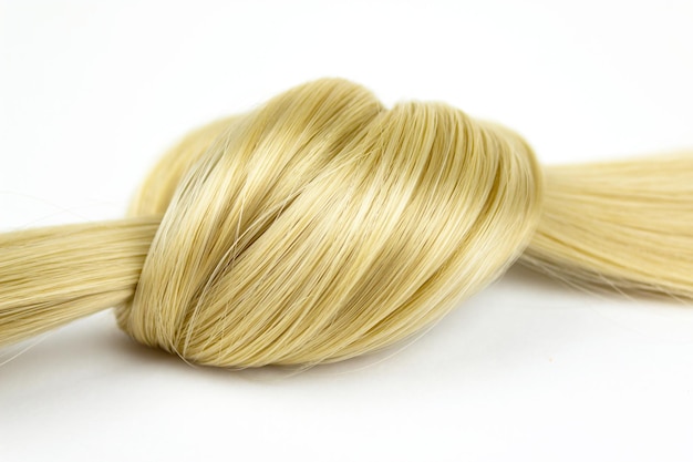 Strand of blond silky hair lock tied in knot on a white background