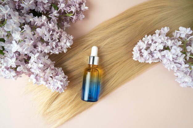 A strand of blonde hair a dropper bottle of natural essential oil for hair treatment