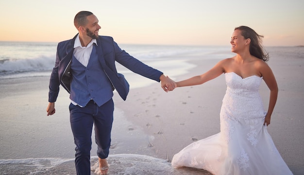 Strand bruiloft huwelijksfeest en paar hand in hand tijdens het wandelen door de zee na liefdesevenement met bruid en bruidegom in de natuur Man en vrouw op wandeling langs de oceaan na ceremonie met glimlach