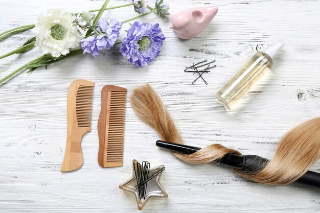 Прядь волос с цветами, парикмахерское оборудование и инструменты на светлом деревянном фоне