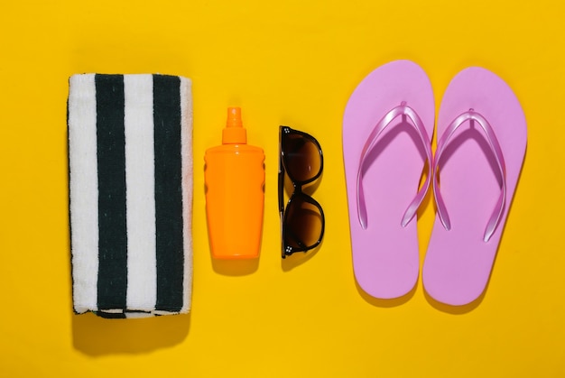 Foto strand vakantie. handdoek, zonnebril, slippers en sunblock-fles op felgeel