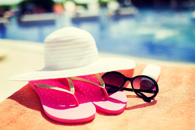 strand, zomer, vakantie en accessoires concept - close-up van hoed, zonnebrandcrème en zonnebril bij het zwembad