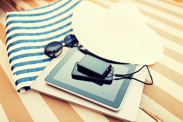 strand, zomervakanties en technologieconcept - close-up van tablet-pc, notebook, smartphone en zomeraccessoires op het strand