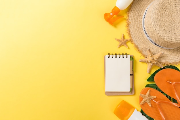 Strandaccessoires met strohoed, zonnebrandfles en seastar op gele achtergrond bovenaanzicht met kopieerruimte.