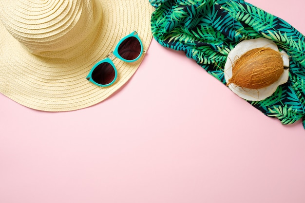 Foto strandaccessoires voor dames: strohoed, zonnebril, kokosnoot, groene sjaal op roze achtergrond. het concept van het reizigersmateriaal, de zomerachtergrond met exemplaarruimte.