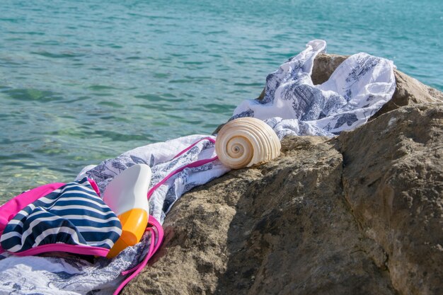 Strandartikelen badkleding zonnebrandcrème en een schelp op een kustrots