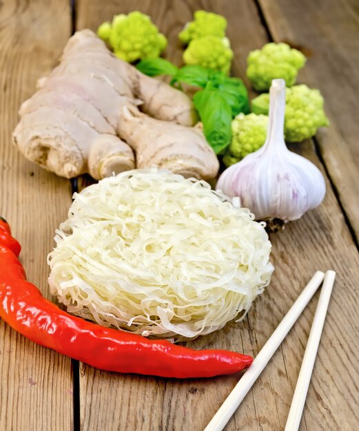 Мель рисовая лапша с чесноком, красным перцем, имбирем и базиликом, брокколи, палочками для еды на фоне деревянных досок