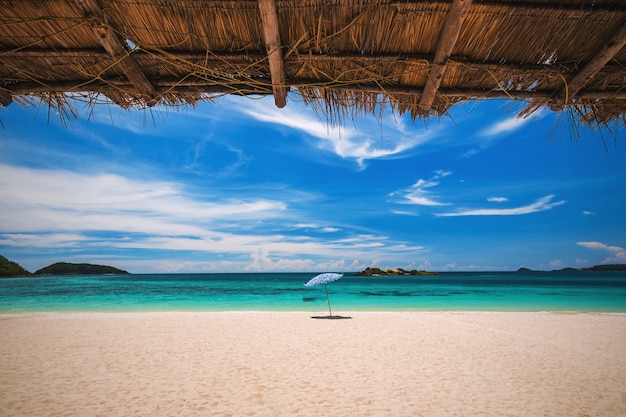 Strandparaplu met smaragdgroene overzees op een zonnige dag, eiland op achtergrond, Thailand