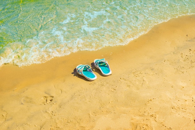 Strandslippers aan de blauwe zeekust met helder waterschelpenzand.