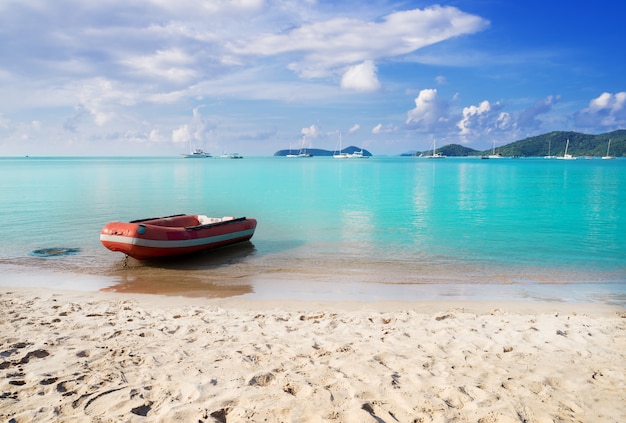 Strandzand en blauwe overzees met boot in blauwe hemel