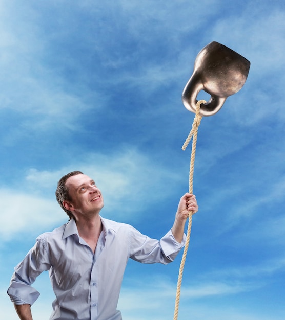 Strange man holds a kettlebell as a ballon against sky