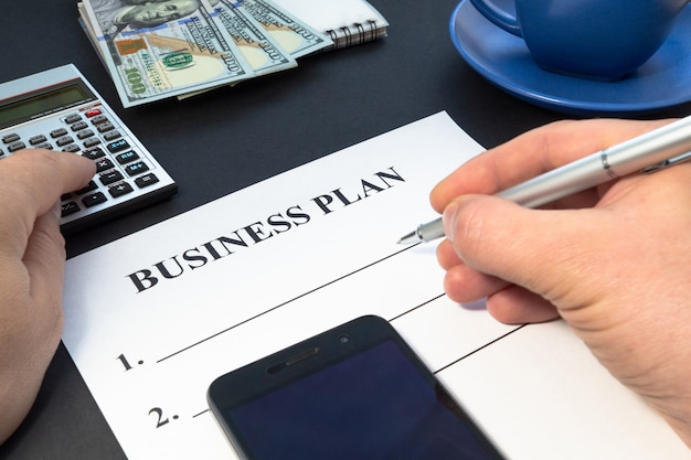 Бизнес-план стратегии с кофе, ручкой и рукой на черном столе