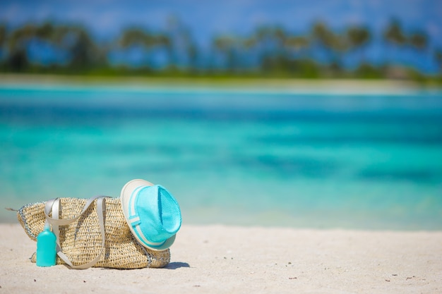 Borsa di paglia, cappello blu, occhiali da sole e bottiglia di crema solare sulla spiaggia tropicale