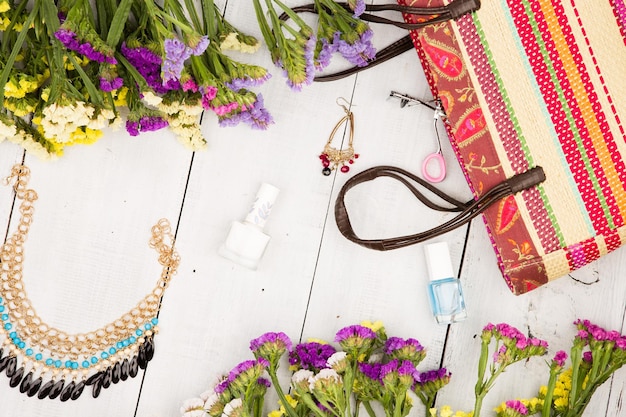 Straw bag colorful flowers cosmetics makeup bijou and essentials on white wooden background