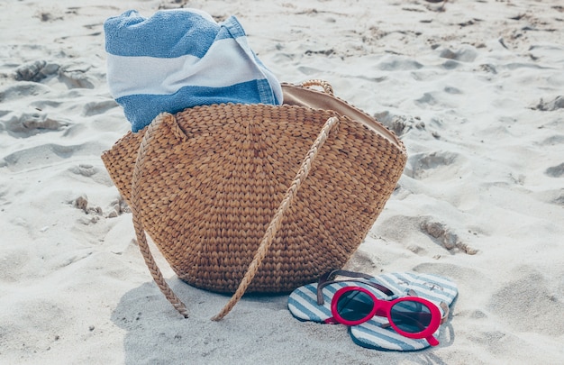 Borsa di paglia, occhiali da sole e infradito su una spiaggia tropicale di sabbia