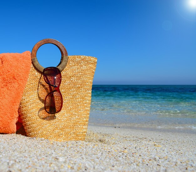 Straw bag towel anad sunglasse by the shore