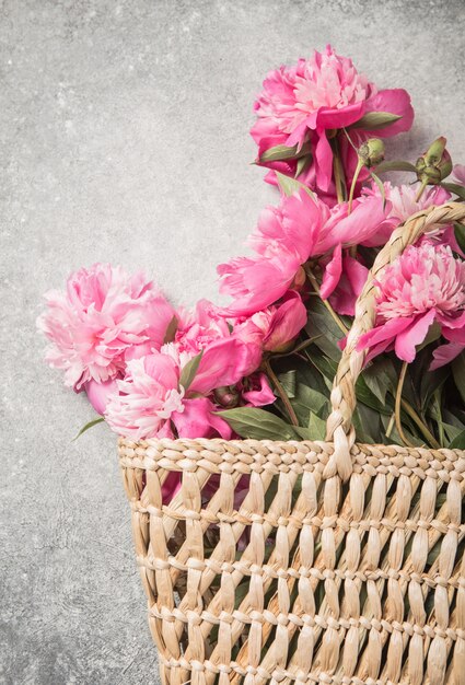 Photo straw bag with pink peony flowers on grey background.