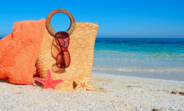 Foto borsa di paglia con occhiali da sole e asciugamano in spiaggia