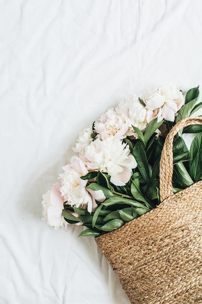 Straw bag with white peony flowers on white surface