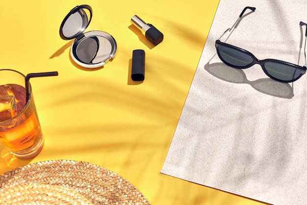 Straw beach woman's hat, beverage with ice in a glass and sunglasses on yellow background