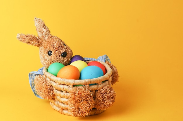 Straw bunny basket with easter colorful eggs on yellow background Happy Easter card Close up
