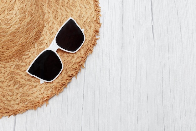 Straw cap and sunglasses on a light wooden background