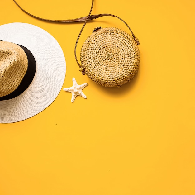 Straw hat, bamboo bag and starfish over yellow background, top view