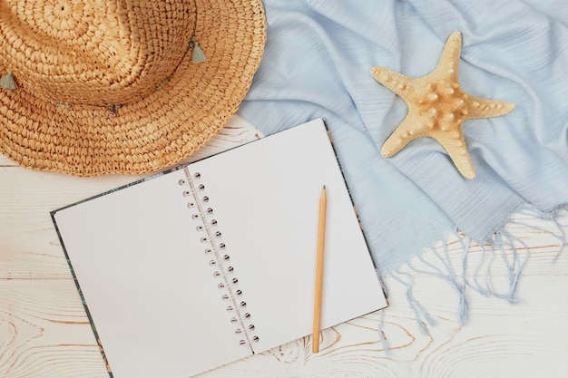 Straw hat blue tippet and starfish and empty diary and pencil on white wooden background summer holiday concept Flat lay