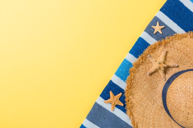 Соломенная шляпа, синее полотенце и морская звезда на желтом фоне. концепция летнего отдыха вид сверху с копией пространства