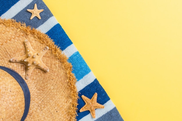 Соломенная шляпа, синий полотенце и морские звезды на желтом фоне. вид сверху концепция летнего отдыха с копией пространства