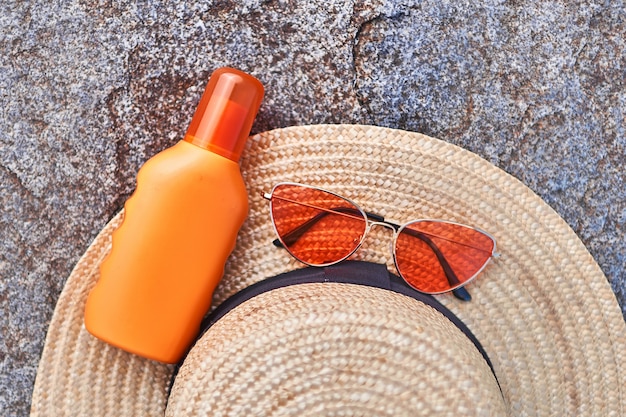 Photo straw hat, bright red glasses and orange bottle of sunscreen for sun protection