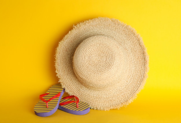 Straw hat and flip flops on color background