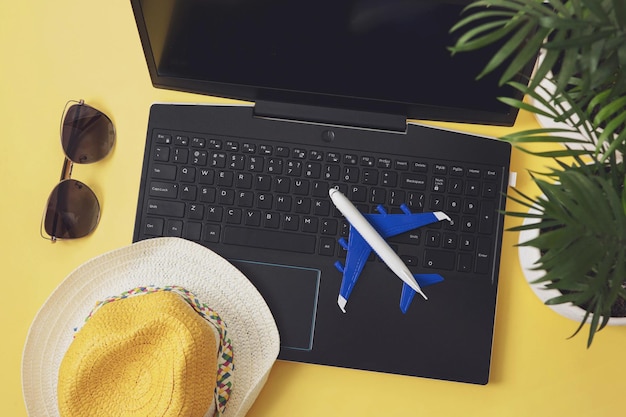 Straw hat, model plane, laptop, sunglasses with leaves of palm on yellow background. Summer holiday, vacation, planning travel concept. Flat lay, top view.